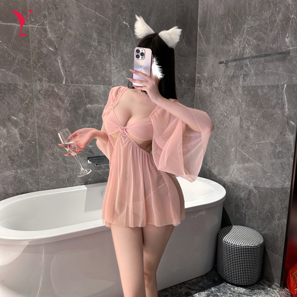 A woman poses in a bathroom wearing a pink sheer mesh sleep dress with an open-crotch design, holding a glass of champagne wh...