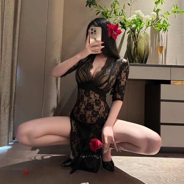 A woman poses in a luxurious setting, wearing a black lace dress with high slits and floral details. the elegant design featu...