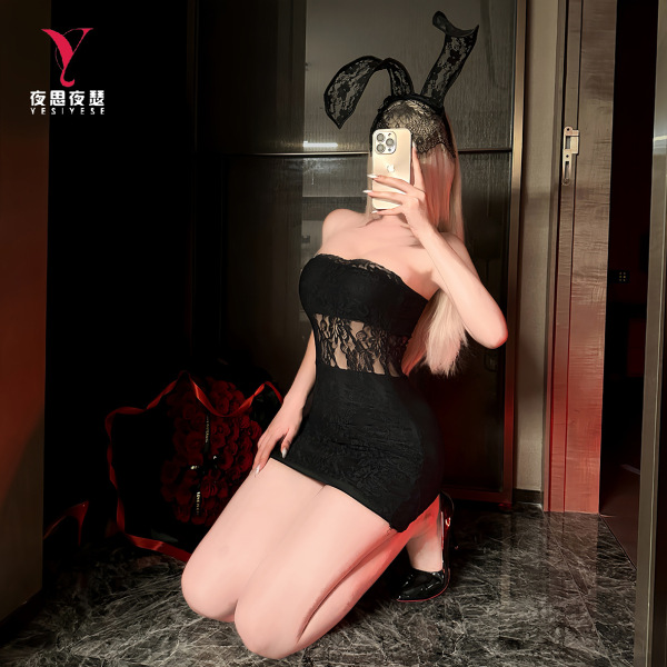 Woman kneeling in black lace bodysuit and sheer mesh skirt set with bunny ears headband, holding phone to face.