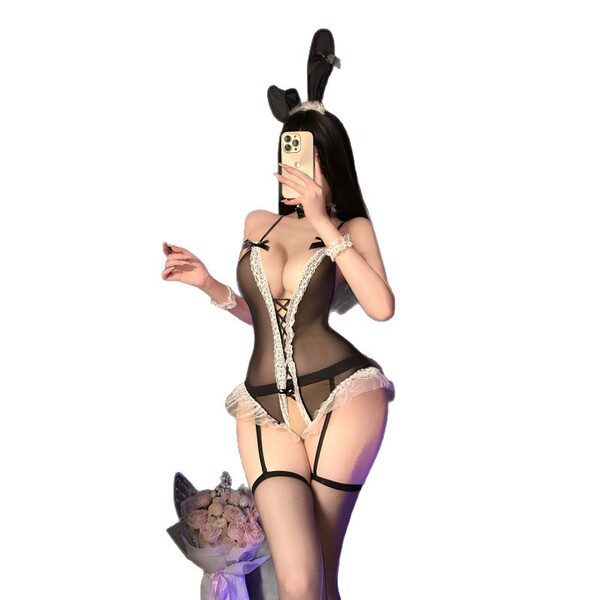 Woman in black sheer lace bunny bodysuit with ties and open-crotch design, holding phone for selfie.