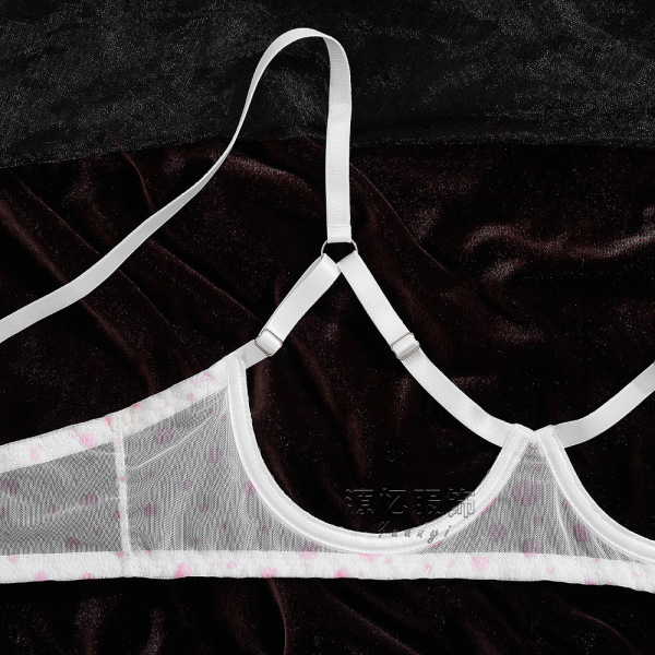 Sheer white bra with pink polka dots and delicate straps on dark velvet background.