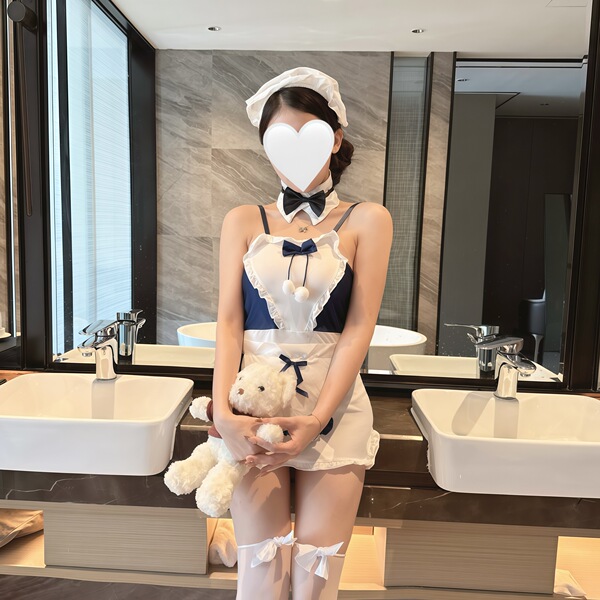 A woman models a maid costume with a white apron, bow tie, and headpiece, holding a teddy bear. the outfit features lace deta...