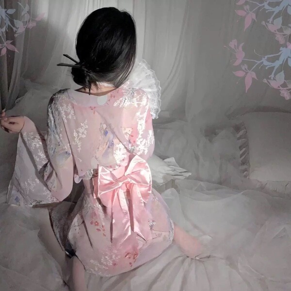 A woman sits on a bed wearing a plus-size japanese-inspired sheer kimono sleep dress. the delicate lace trim and sensual desi...