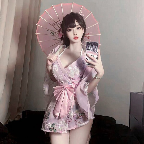 Woman in pink sheer kimono lingerie set with bow print, holding parasol and phone, posing indoors.