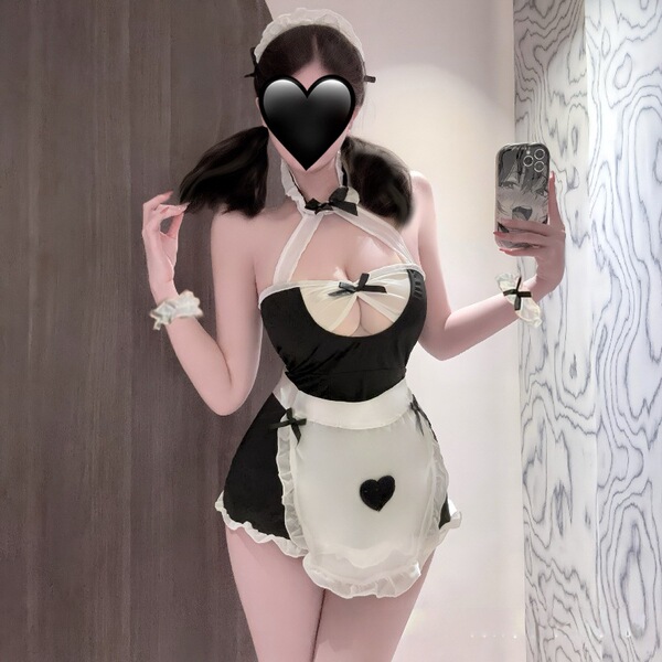 Woman wearing black and white plus size maid costume with apron, bow tie, and heart details, holding phone for selfie.