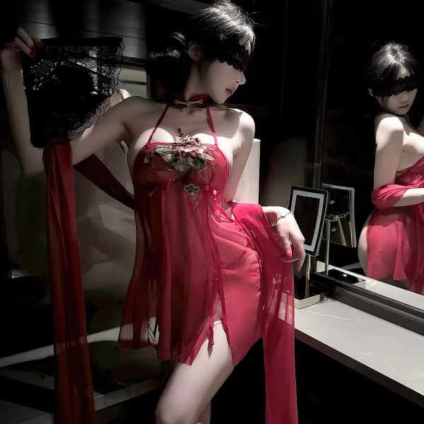Woman wearing red sheer lace sleep dress with vintage embroidery, holding matching lingerie in dimly lit room.