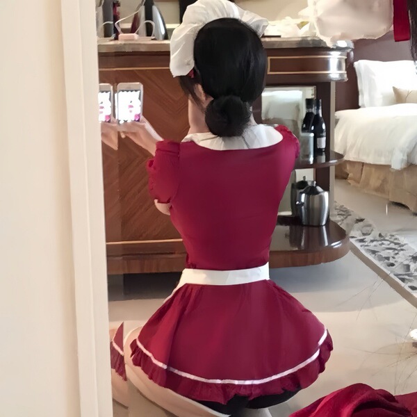 A woman wearing a red maid costume with a white apron, featuring ruffled details and a bun hairstyle, captured from behind.