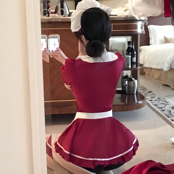 A woman wearing a red maid costume with white apron, captured from behind as she takes a photo in a room setting.