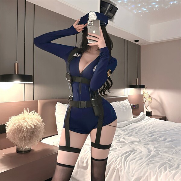 Woman in navy blue role play bodysuit with harness, thigh straps, and cap, posing in bedroom mirror.