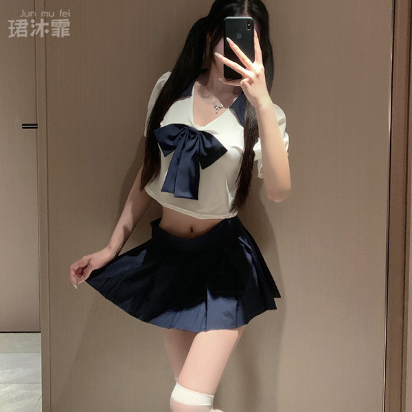 A person wearing a white crop top with a navy blue bow and pleated skirt, paired with sheer stockings, posing for a mirror se...