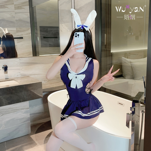 A person wearing a bunny-themed schoolgirl outfit, featuring a navy blue swimsuit with white accents and bunny ears, posing p...