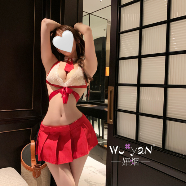 Woman wearing red and white pure & playful lingerie set with jk-style skirt, lace bralette, and bow accents in modern room.