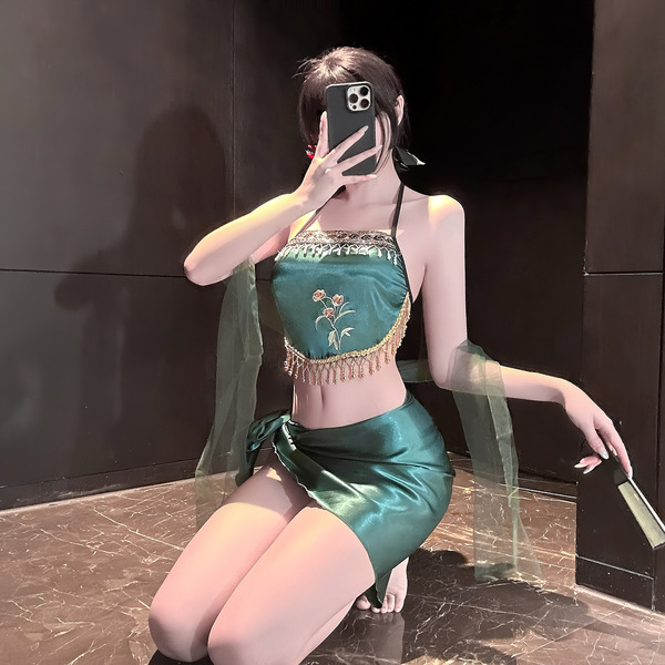 A woman poses with a smartphone, wearing a green, exotic-style bralette top adorned with floral embroidery and fringe details...