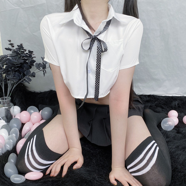 A person models a playful schoolgirl-inspired set featuring a white shirt with a black polka dot bow tie, paired with a pleat...