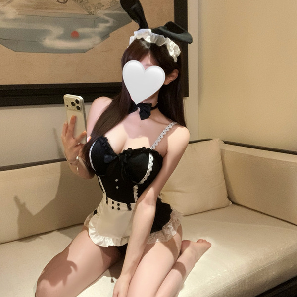Woman in elegant maid costume with lace details, posing on a beige sofa. pure & seductive lingerie set - sensual playwear.