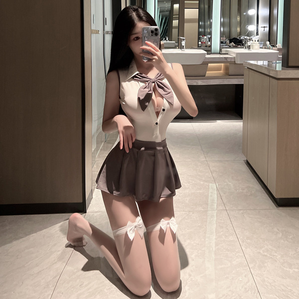 A woman poses in a bathroom wearing a sexy backless jk schoolgirl outfit from pure temptation, featuring a bow tie and skirt,...