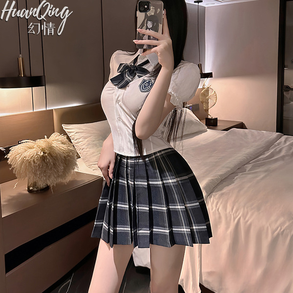 A woman poses in a bedroom wearing a cute japanese school uniform set, featuring a plaid skirt and blouse with a bow tie. the...