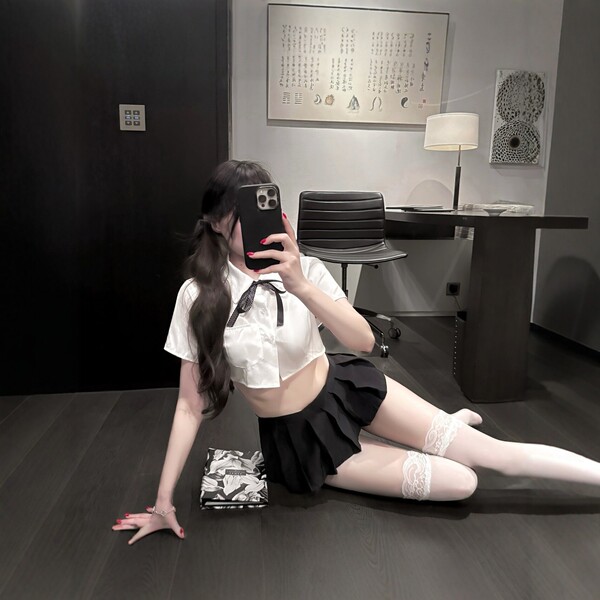 A woman poses seductively in a modern room, wearing a white blouse with a black skirt, lace stockings, and holding a phone. t...