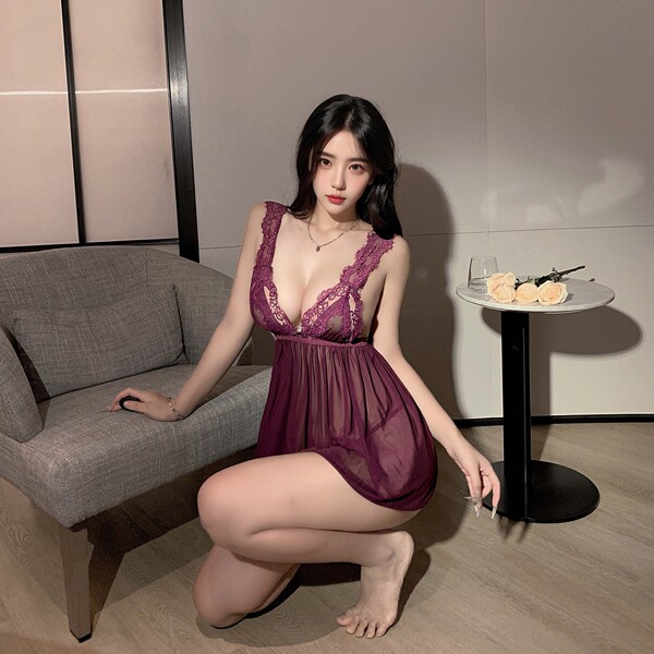 Woman wearing pure & tempting deep v lace sleep dress with sheer mesh and high slit, posing beside sofa in soft lighting.