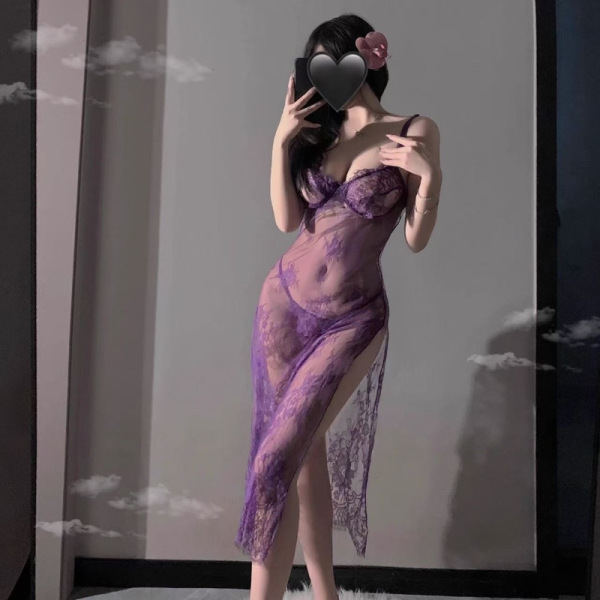 Woman wearing purple lace lingerie set with sheer straps, slit skirt, and floral hair accessory in soft lighting.