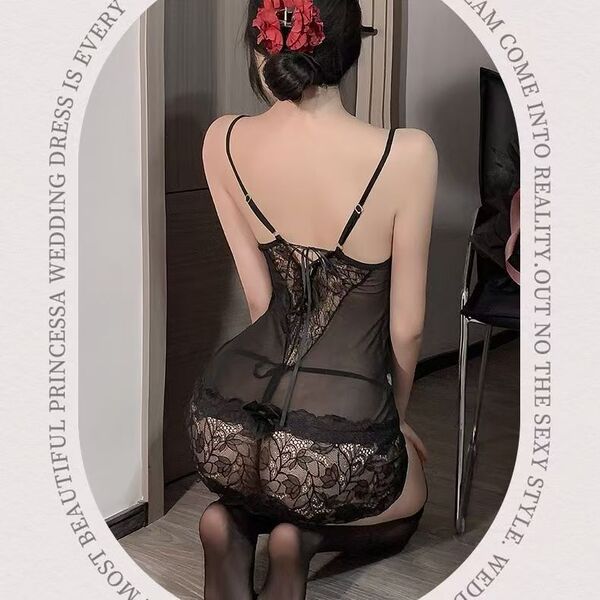 Woman wearing sheer black lace lingerie sleep dress with floral details, viewed from behind in a bedroom setting.