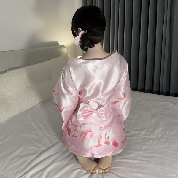 A woman sits on a bed wearing a pink qiaoduo temptation kimono set, featuring anime-inspired designs and lace details. the si...