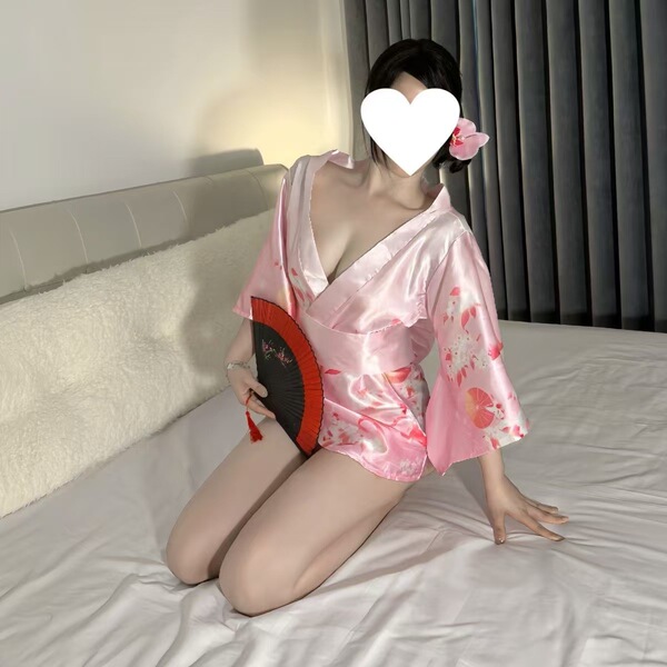 A woman poses on a bed wearing a pink qiaoduo temptation kimono set, featuring anime-inspired designs and lace details. she h...