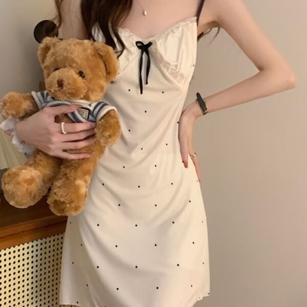 A woman holds a teddy bear while wearing a cream cherry print cami slip dress with lace trim and built-in pads, exuding elega...