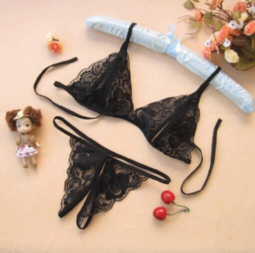 Black lace thong bra set with sheer open-crotch design, displayed with decorative cherries and a small doll.