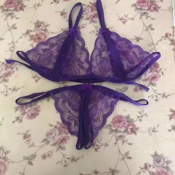 Purple lace thong bra set with sheer open-crotch design, displayed on floral fabric background.