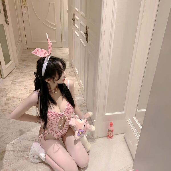 Woman in pink rabbit girl lingerie set with bunny ears, holding plush toy, kneeling on marble floor.