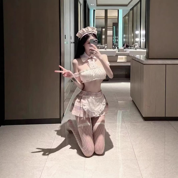 A woman poses playfully in a bathroom, wearing a maid-themed outfit featuring a lace bodysuit, sheer mesh stockings, and a ma...