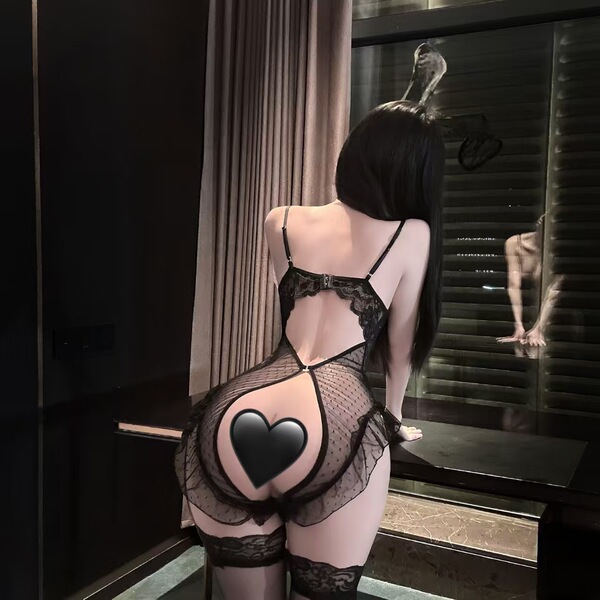 Woman wearing seasonal seductive lace bodysuit, sheer mesh with pearl chain detail, posing by window.