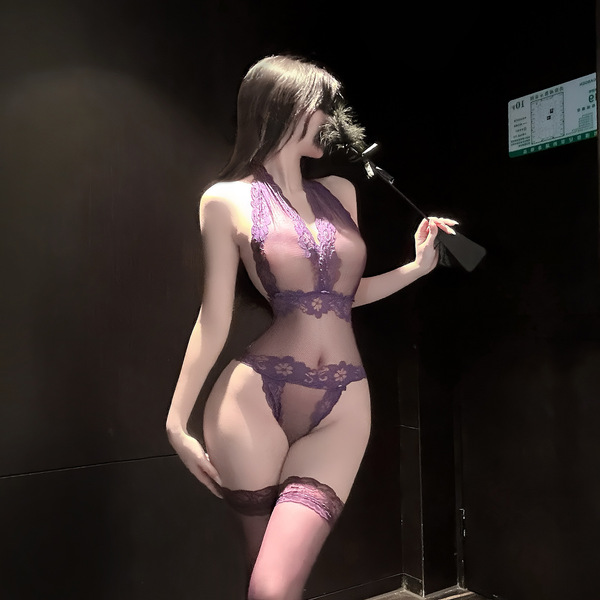 Woman wearing purple lace lingerie set with sheer top, thong, and thigh-high stockings in dimly lit room.