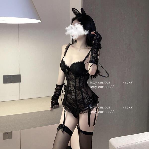 Woman wearing black lace lingerie set with sheer mesh bodysuit, garter stockings, and cat ears in modern room.