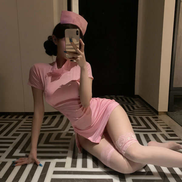 Woman in pink nurse costume lingerie set posing on floor, featuring short dress, lace stockings, and matching hat.