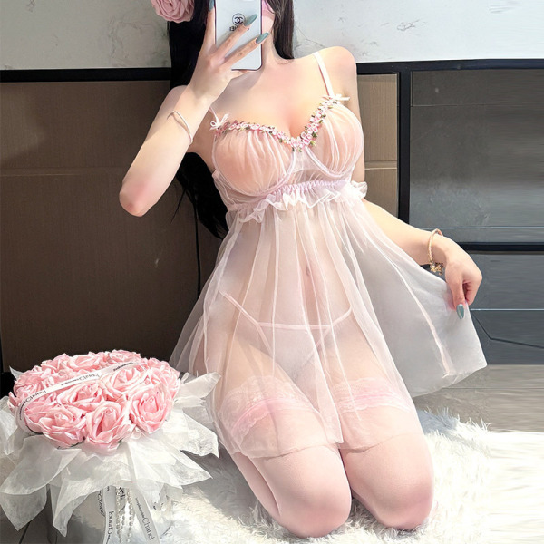 Woman kneeling in pink sheer mesh lingerie set with lace trim, holding phone for mirror selfie beside bouquet of roses.