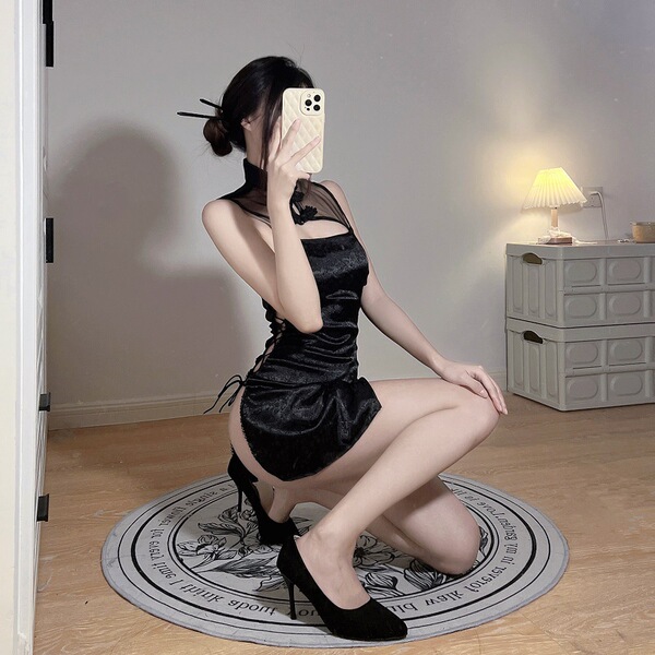 Woman posing in black sheer cheongsam lingerie set with high heels, sitting on circular rug indoors.