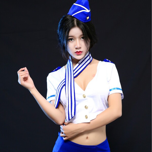 Woman modeling a sexy airline hostess costume set with blue hat, white top, and scarf for playful roleplay.