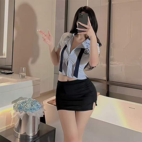 Woman wearing a tight, sexy female police officer costume with short skirt and tie, posing in a modern bathroom setting.