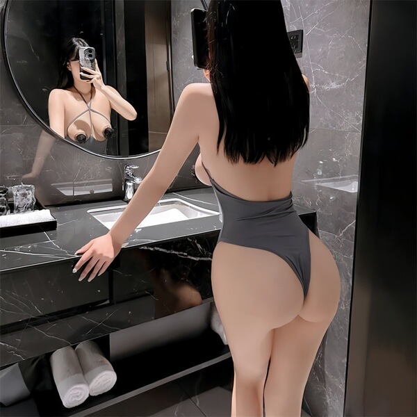Woman in sexy lace bodysuit with open-crotch design, posing in modern bathroom mirror for seductive sleepwear look.