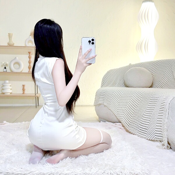 A woman in a white sheer mesh sexy lace cheongsam lingerie set poses seductively while taking a photo, showcasing the elegant...