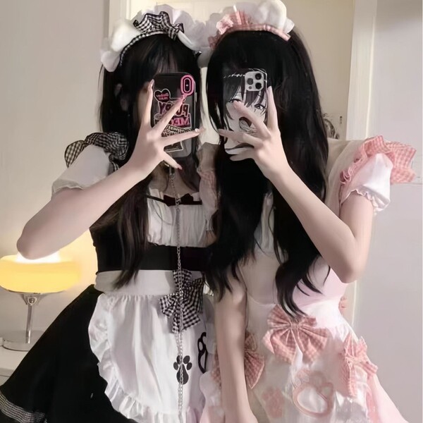 Two individuals wearing matching black and white maid costumes with bows, posing for a mirror selfie. the outfits feature ruf...