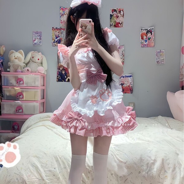 A person wearing a pink maid costume with ruffles and bows, taking a mirror selfie. the outfit features playful details suita...