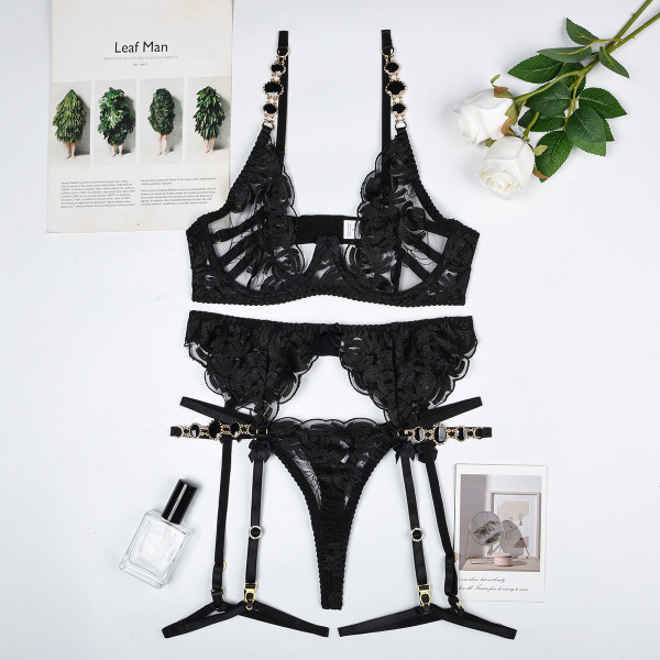 Black lace lingerie set with bra, thong, and garter straps displayed flat lay with roses and perfume.
