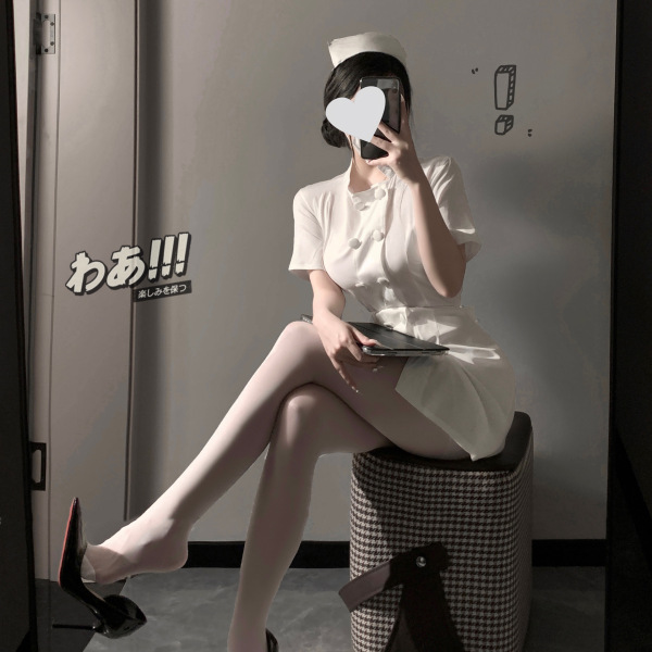Woman in white nurse costume with bow-tie skirt and round neck top, sitting on stool, holding phone, wearing high heels.