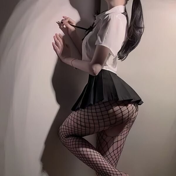 Woman in sexy jk-style uniform set with ultra-short skirt, crop top, and fishnet stockings posing against wall.