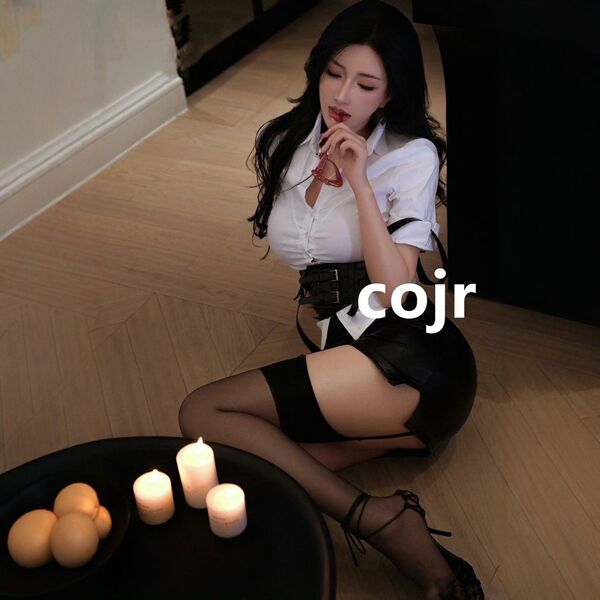 Woman in sexy secretary outfit set with white blouse, black skirt, and stockings, posing seductively by candlelight.