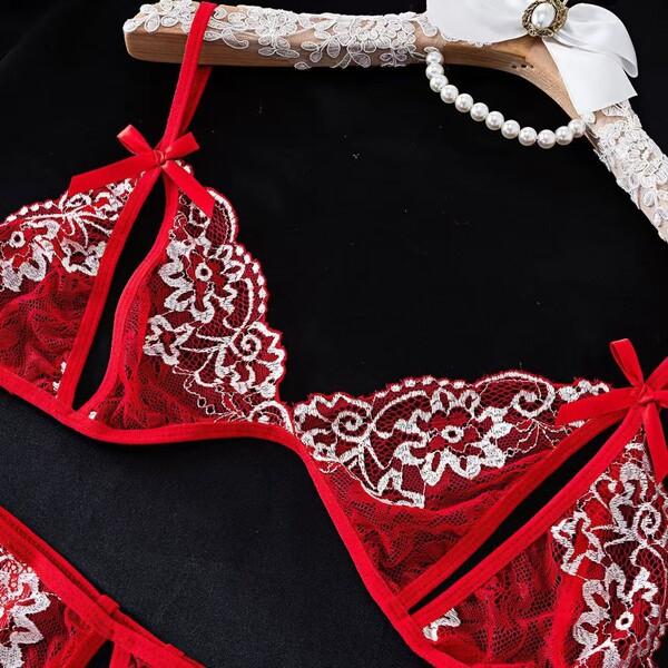Red lace lingerie set with floral embroidery and ribbon details, displayed on a hanger with pearls.