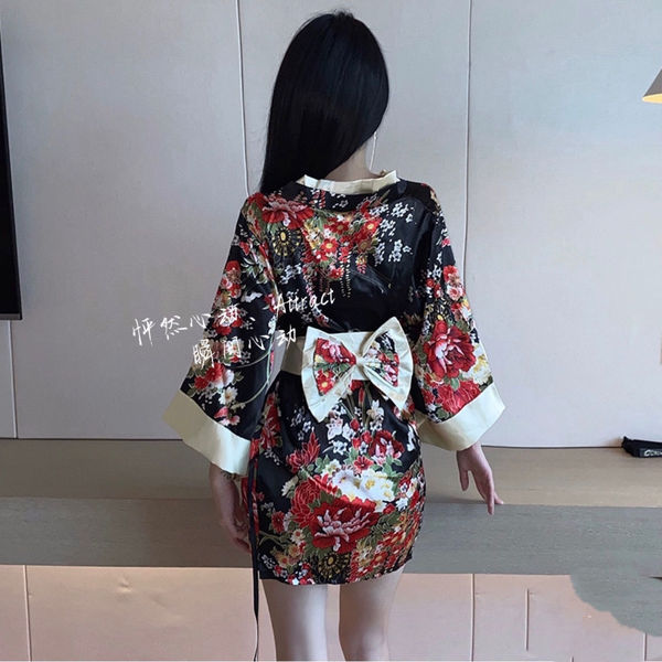 A woman stands facing away from the camera, wearing a black floral-patterned shōwa geisha robe. the dress features a deep v-c...